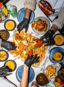 A group of people enjoying a seafood boil with different sauces at Hot n Juicy Shrimp LDN. A hands-on feast featuring shrimp, crab, mussels, and corn, drenched in buttery, garlicky, and spicy flavors. The ultimate seafood experience in London.